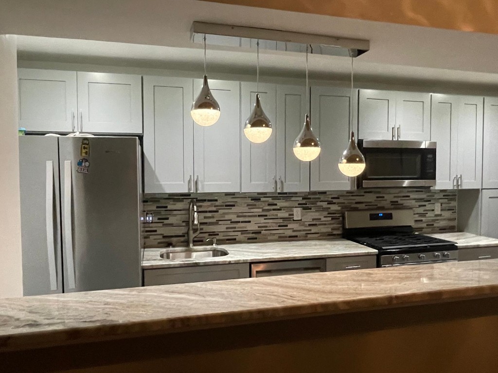Completed kitchen — grey shaker cabinets, marble counters, and pendant lighting