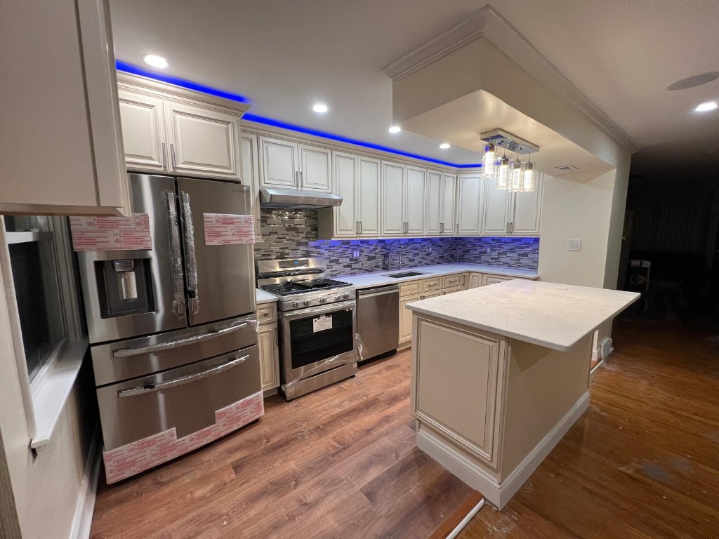 Finished kitchen — stainless appliances, cream cabinetry, and island lighting